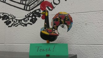 Rooster with Paper That Says Teach