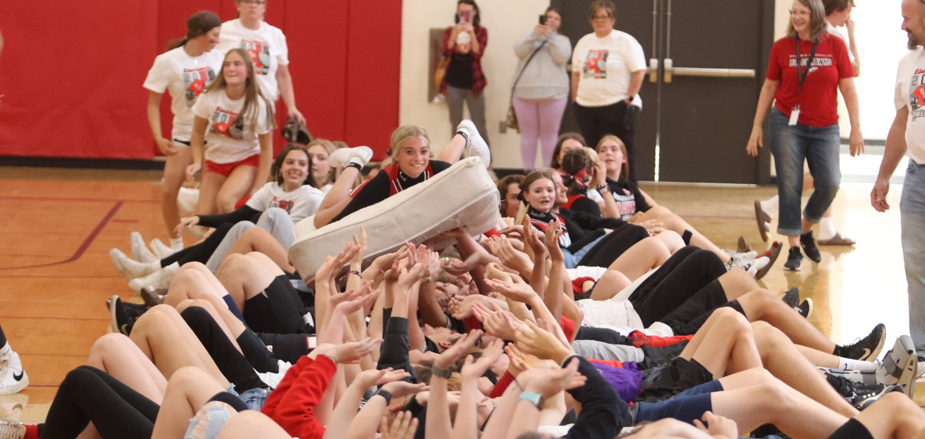 Student riding on a mattress lifted by students at pep fest.